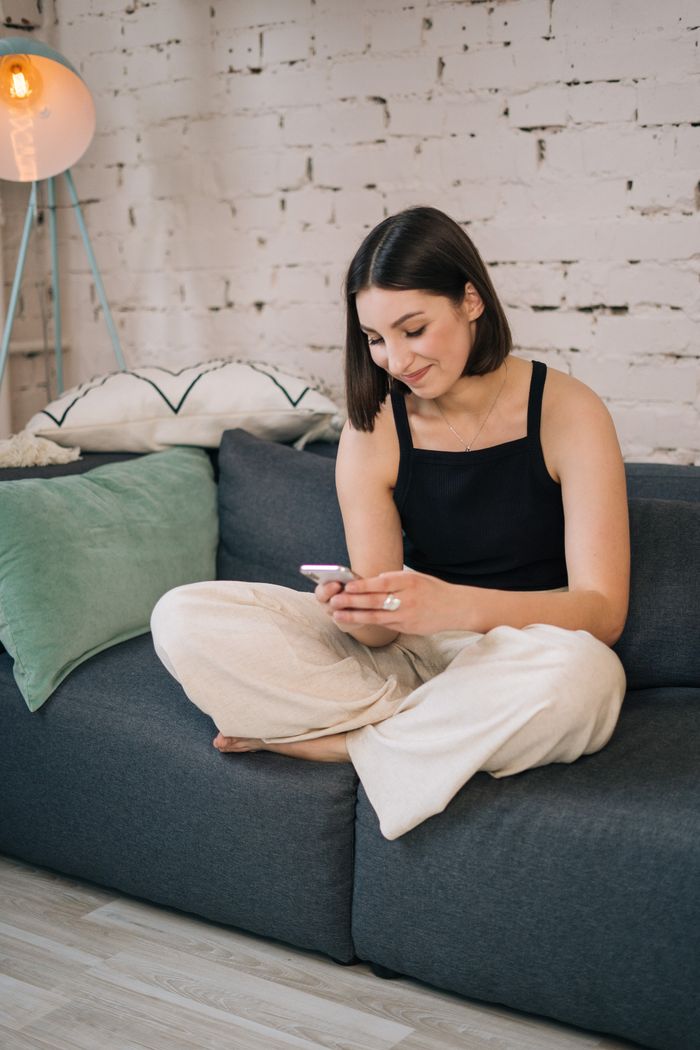 about-01 A young woman sits comfortably on a sofa, engrossed in her smartphone.